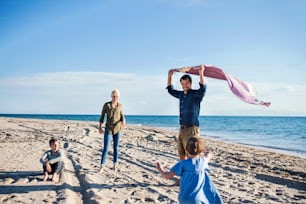 Junge Familie mit zwei kleinen Kindern, die barfuß im Freien am Strand spazieren gehen und Spaß haben.