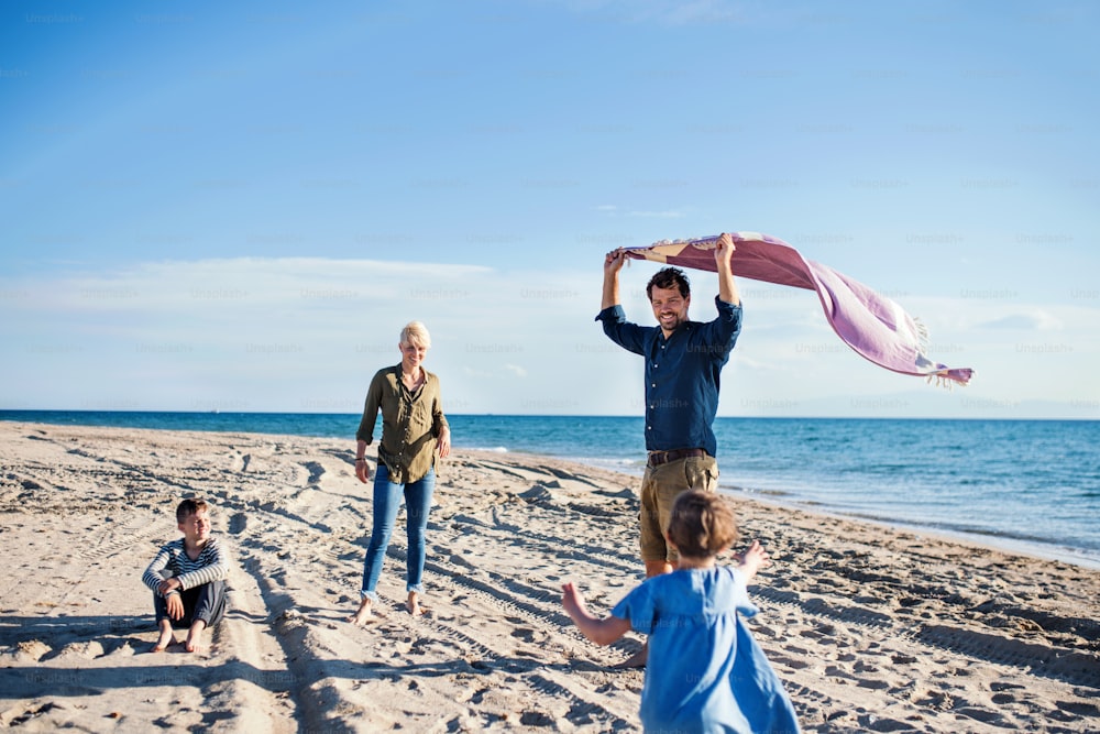 Junge Familie mit zwei kleinen Kindern, die barfuß im Freien am Strand spazieren gehen und Spaß haben.