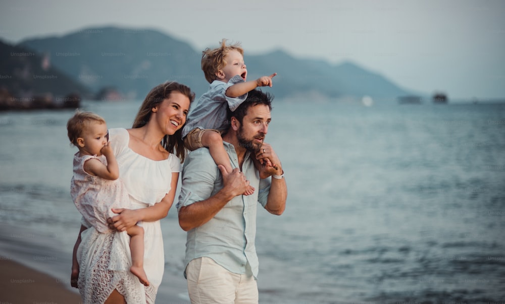Eine junge Familie mit zwei Kleinkindern, die in den Sommerferien am Strand steht und lacht.