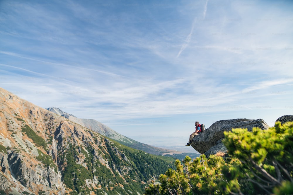夏に山をハイキングし、岩の上で休むバックパックを背負った成熟した男性。