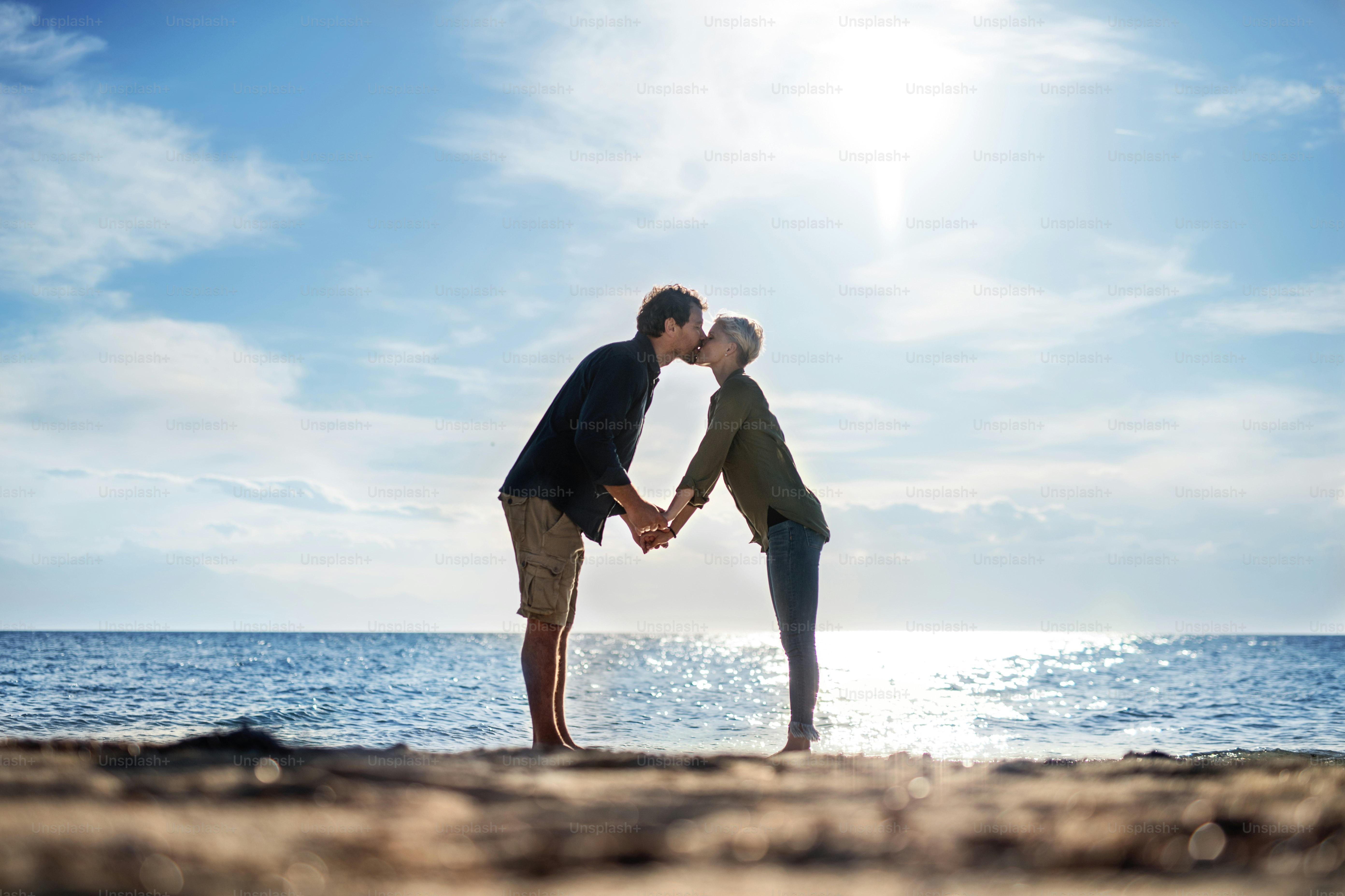 Um jovem casal de pé ao ar livre na praia, se beijando. Espaço de cópia.