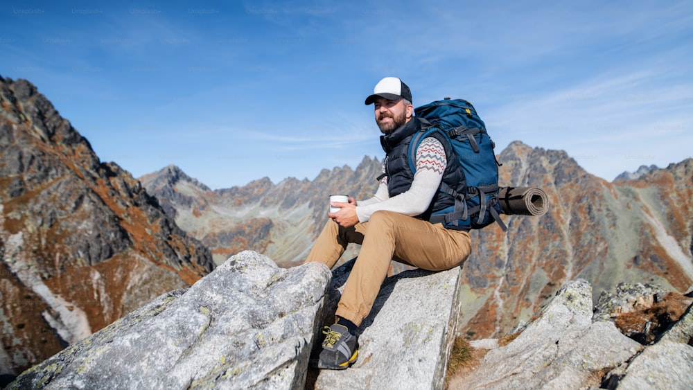 Mature man with backpack hiking in mountains in autumn, resting on rock.