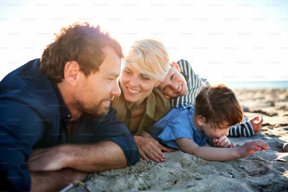 Porträt einer jungen Familie mit zwei kleinen Kindern, die draußen am Strand liegen und sich ausruhen.