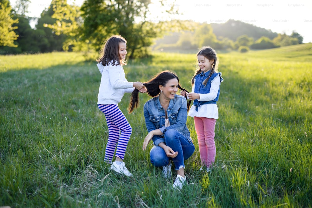 Vorderansicht der Mutter mit zwei kleinen Töchtern, die Spaß im Freien in der Frühlingsnatur haben und mit Haaren spielen.
