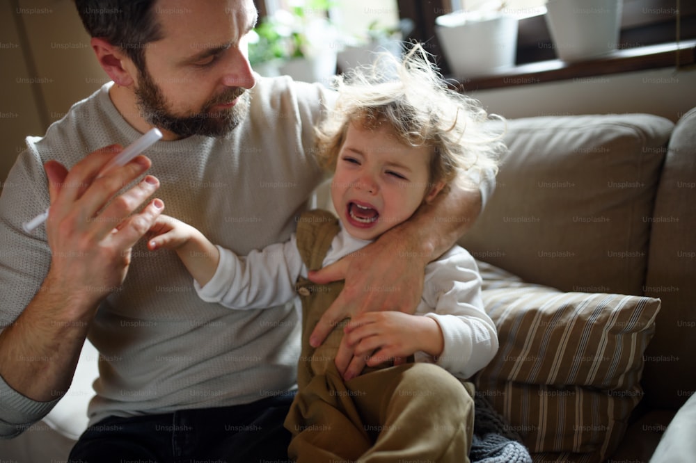 Vista frontal do pai maduro dando xarope para a pequena filha doente dentro de casa.