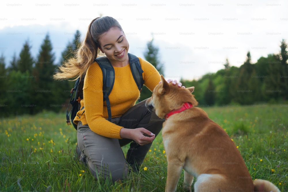 Giovane donna felice con un cane durante una passeggiata all'aperto nella natura estiva.