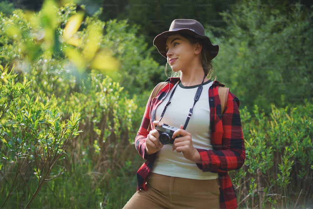 Frontansicht einer jungen Frau mit Kamera auf einem Spaziergang im Wald in der Sommernatur, stehend.