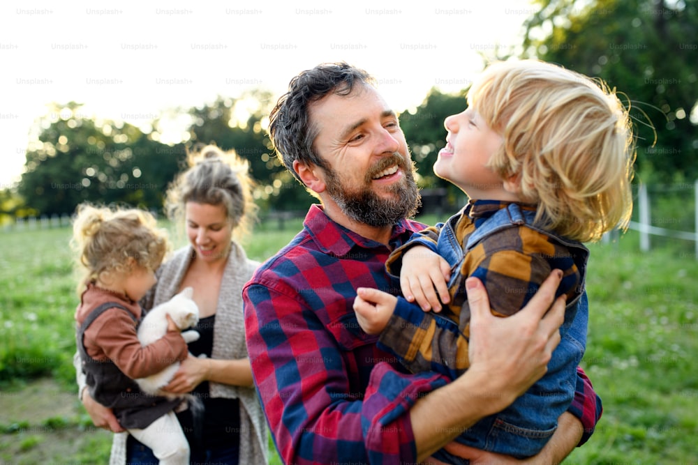Porträt einer glücklichen Familie mit kleinen Kindern, die auf dem Bauernhof stehen und sich ausruhen.