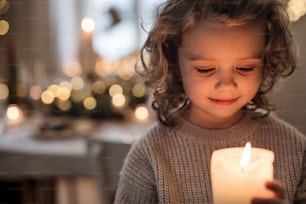 Portrait of cheerful small girl indoors at home at Christmas, holding candle.