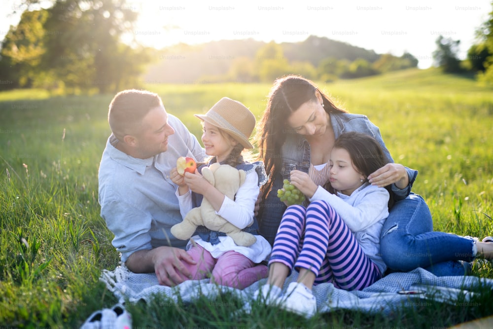 Front view of happy family with two small daughters sitting outdoors in spring nature, having picnic.