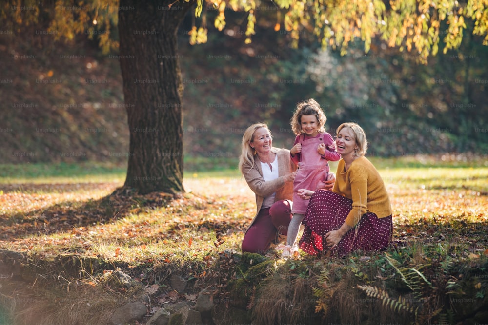 Portrait of small girl with mother and grandmother resting in autumn forest.
