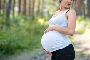 Unrecognizable happy pregnant woman outdoors in nature, touching her belly.