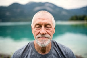 A front view portrait of senior man pensioner standing outdoors in nature, eyes closed.