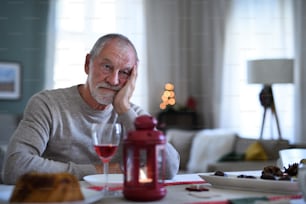 クリスマスに屋内のテーブルに座っているワインを持つ孤独な老人の肖像画、孤独のコンセプト。
