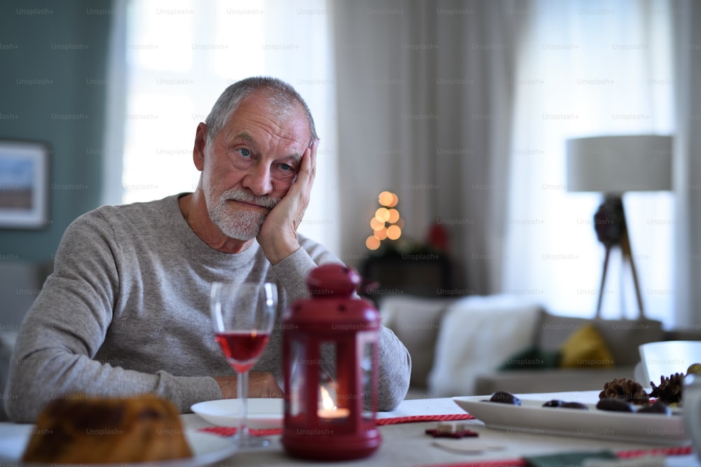 Porträt eines einsamen älteren Mannes mit Wein, der an Weihnachten drinnen am Tisch sitzt, Einsamkeitskonzept.