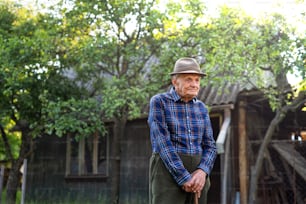Um retrato de um homem idoso em pé ao ar livre no jardim, descansando.