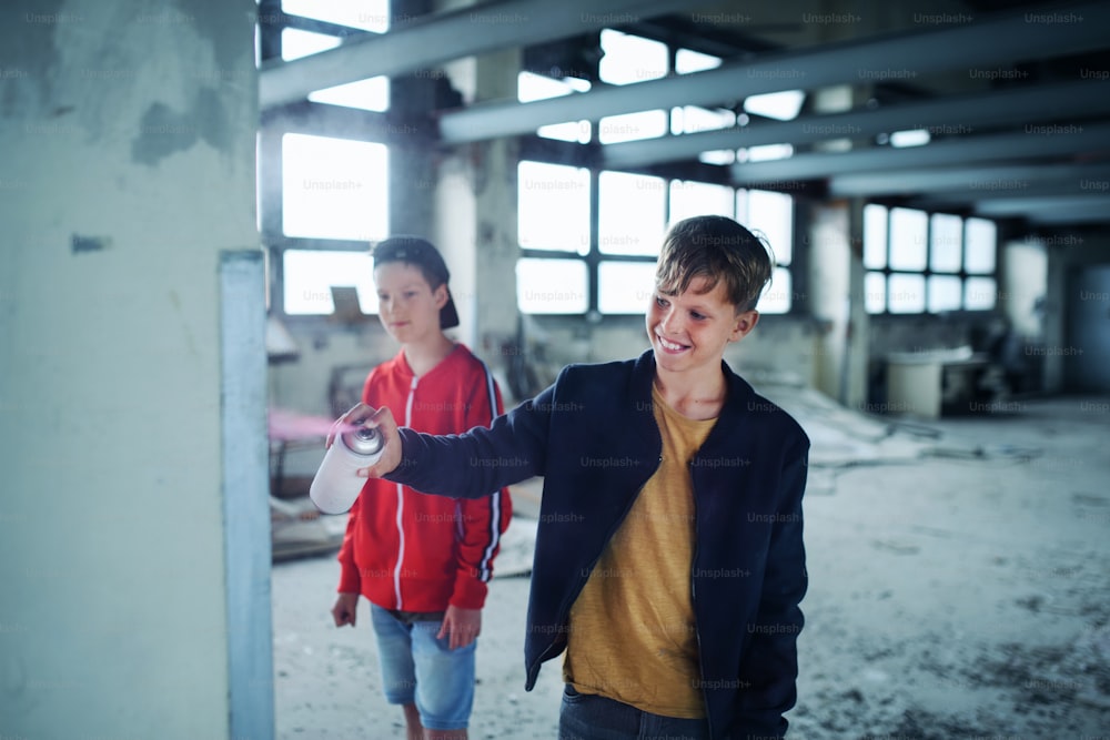 Group of teenagers boy gang standing indoors in abandoned building, using spray paint on wall.