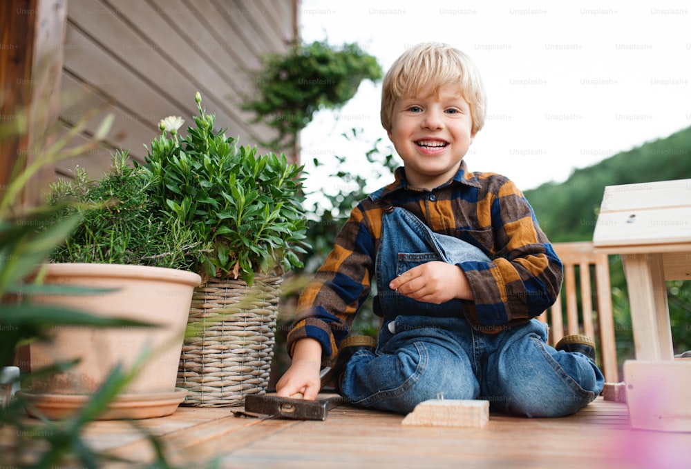 Portrait of happy small boy outdoors on table constructing birdhouse, diy project.