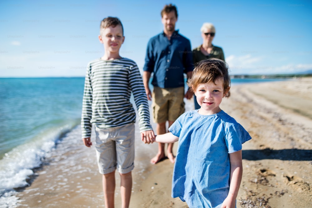 Young family with two small children walking outdoors on beach, holding hands.