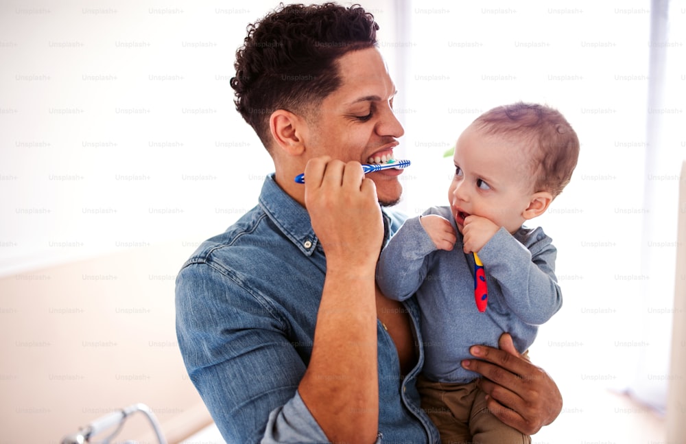 Junger Vater und kleiner kleiner Sohn in einem Badezimmer drinnen zu Hause, Zähneputzen.