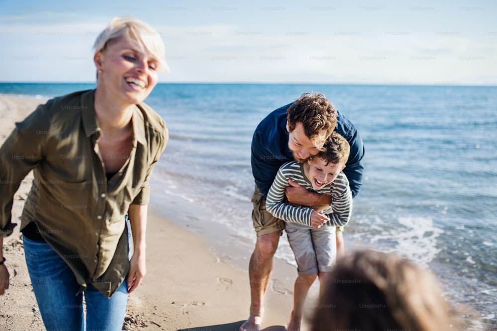 Ritratto di giovane famiglia con due bambini piccoli all'aperto sulla spiaggia, divertendosi.