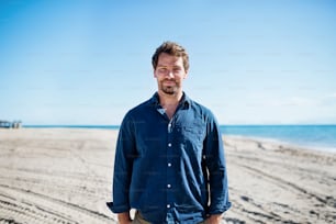 Front view of mature man on a walk outdoors on beach, looking at camera.