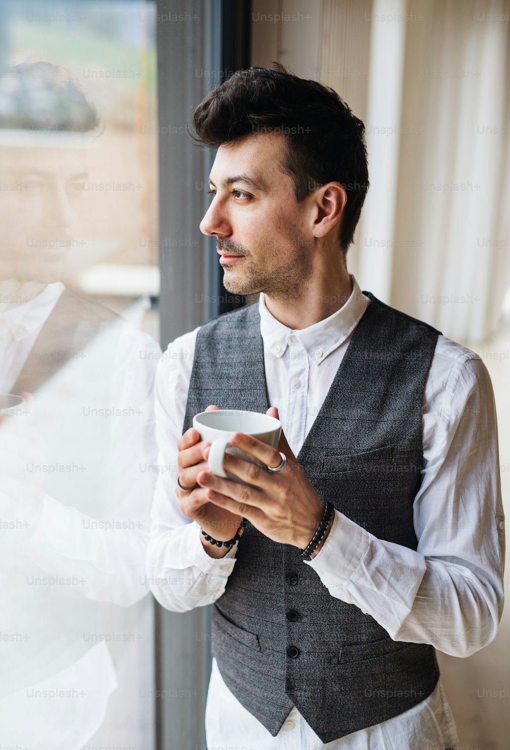 A young man with coffee standing by the window. Copy space.