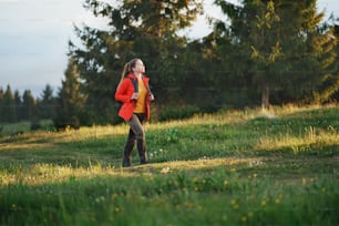 Vista laterale di giovane donna su una passeggiata all'aperto sul prato nella natura estiva, camminando.