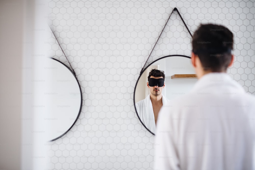Young man with eye mask in the bathroom in the morning, standing in front of mirror.