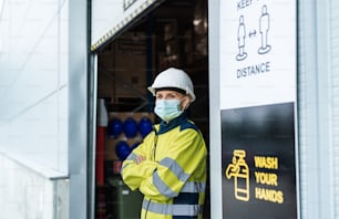 Portrait of woman worker with face mask standing in front of warehouse, coronavirus concept.
