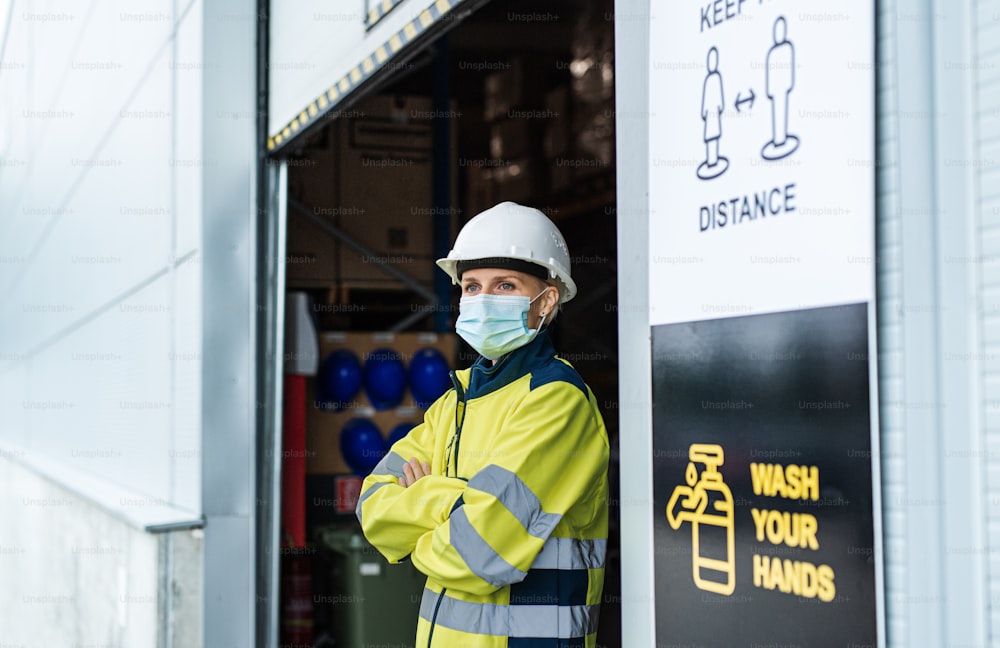 Retrato de mulher trabalhadora com máscara facial em pé em frente ao armazém, conceito de coronavírus.