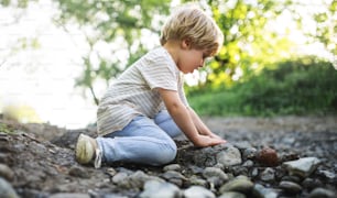 Seitenansicht eines glücklichen kleinen Jungen, der mit Felsen und Schlamm in der Natur spielt.