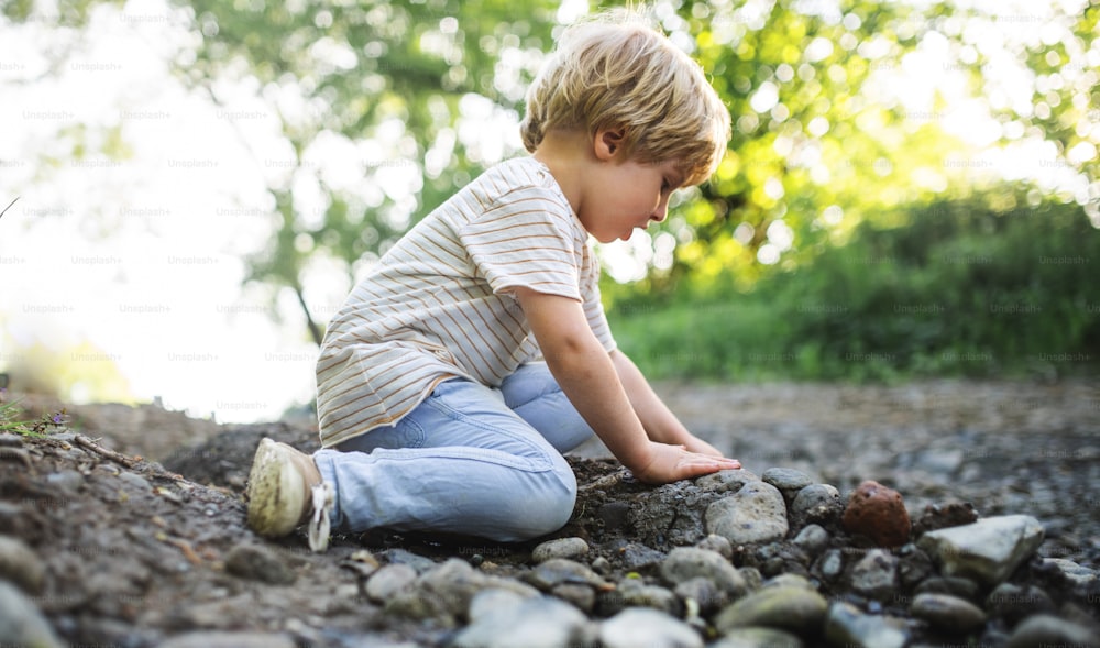 Side view of happy small boy playing with rocks and mud in nature.