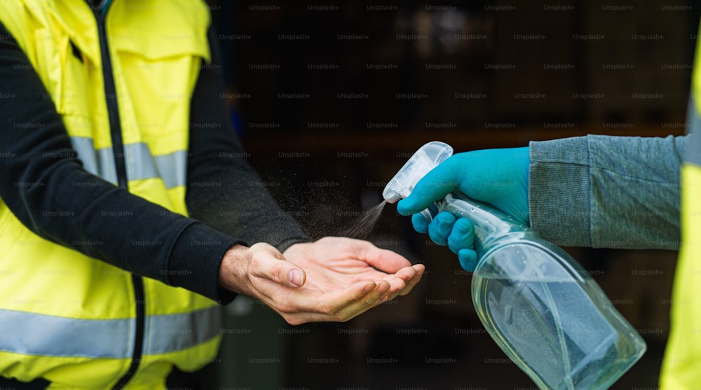 Sección media de trabajadores de almacén irreconocibles desinfectando manos, concepto de coronavirus.