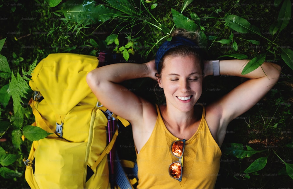 숲 속 야외에서 바닥에 누워 쉬고 있는 행복한 여자 등산객의 상위 뷰.