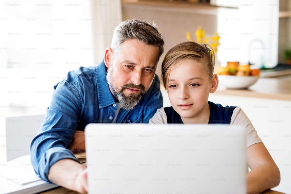 A mature father with small son sitting at table indoors, using laptop.