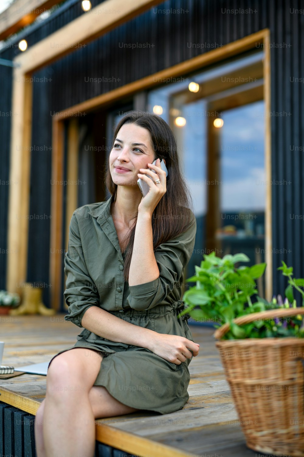Happy young woman with smartphone outdoors, weekend away in container house in countryside.