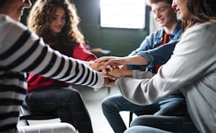 Hombres y mujeres sentados en círculo durante la terapia de grupo, apilando las manos.
