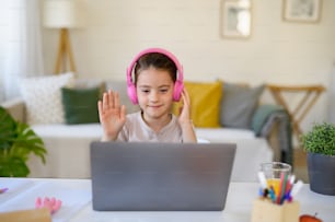 Schoolgirl having online lesson indoors at home, greeting teacher and coronavirus concept.
