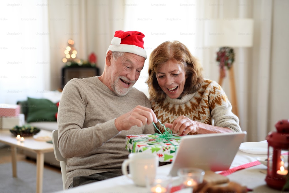 Happy senior couple opening present indoors at home at Christmas, having video call with family.