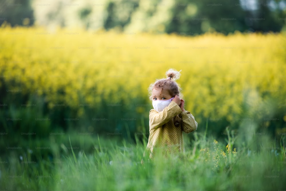 Front view of happy small toddler girl standing in spring nature in rapeseed field.
