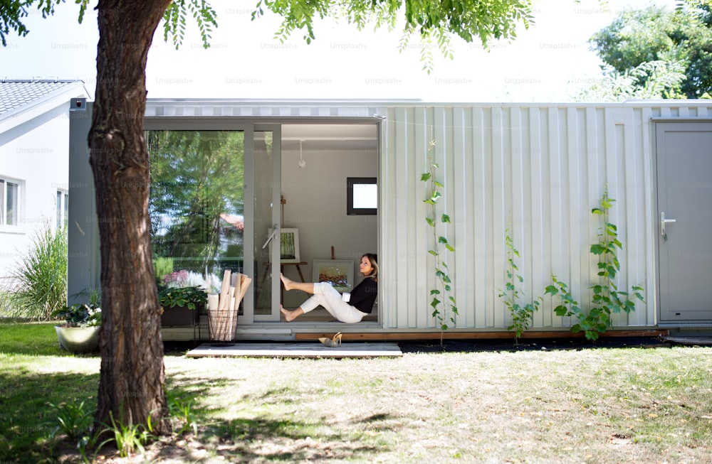 Mature woman with coffee working in home office in container house in backyard, resting.