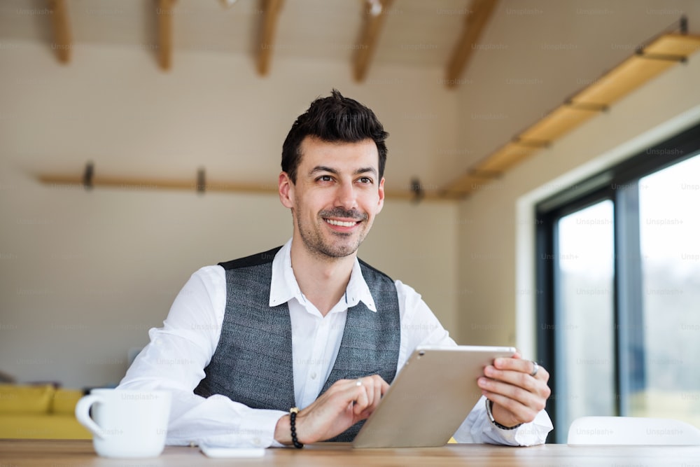 Young handsome man with coffee sitting at the table, using tablet.