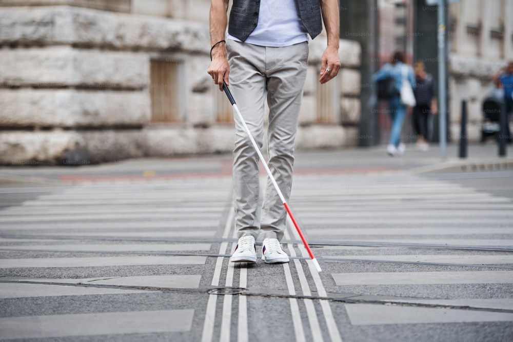 도시의 거리를 가로질러 걷고 있는 흰 지팡이를 짚은 알아볼 수 없는 젊은 장님의 중간 부분.