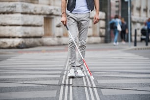 白杖をついた見分けのつ�かない若い盲目の男が街の通りを横切って歩いている。