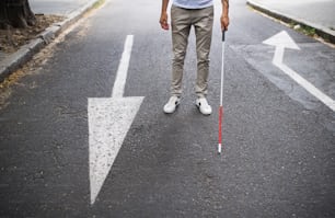Sección media de un joven ciego irreconocible con bastón blanco caminando por la calle en la ciudad.