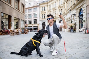 Un joven ciego con bastón blanco y perro guía en la zona de pedestal de la ciudad.