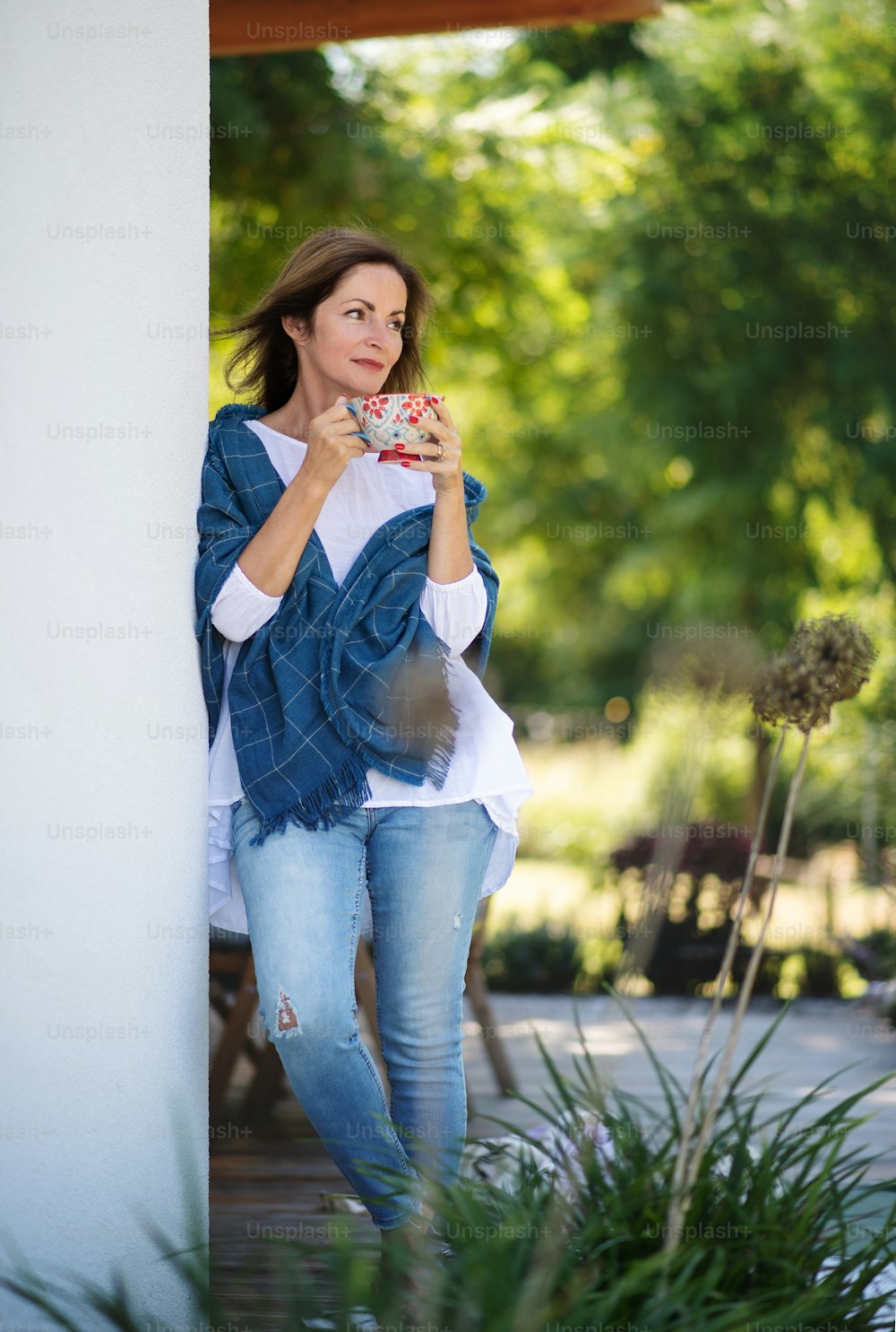 Side view of mature woman with cup of tea resting outdoors in backyard.