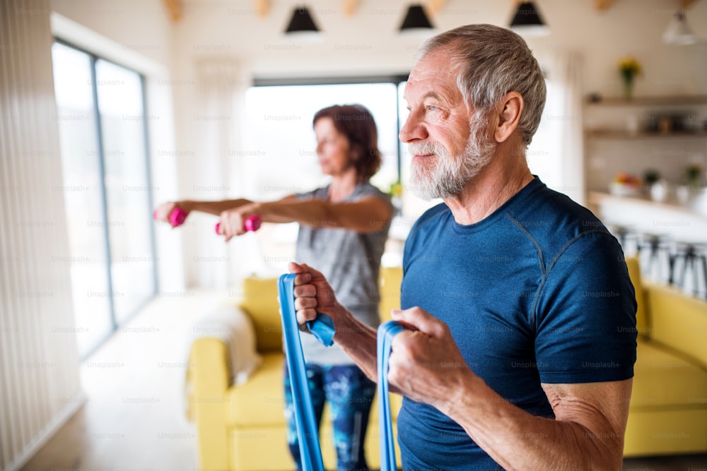 Un couple de personnes âgées heureux à l’intérieur à la maison, faisant de l’exercice à l’intérieur.