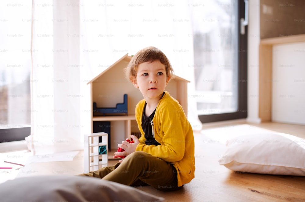 A small girl playing with a wooden house on the floor at home.